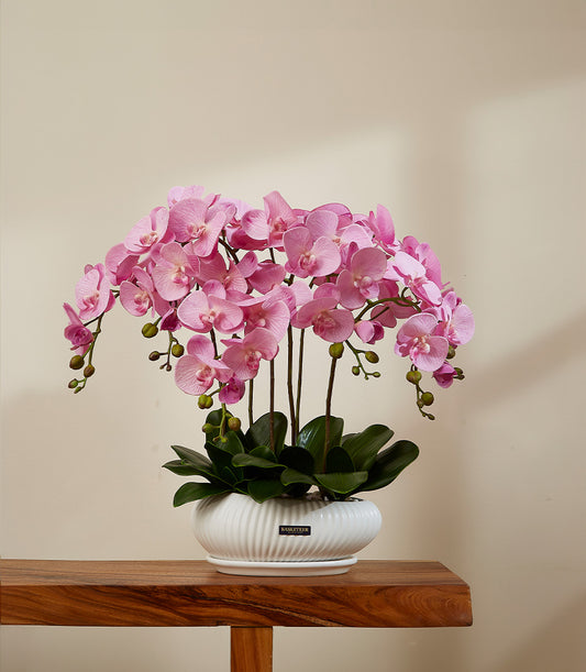 Vibrant pink artificial orchid arrangement in white ribbed ceramic planter with green leaves and saucer