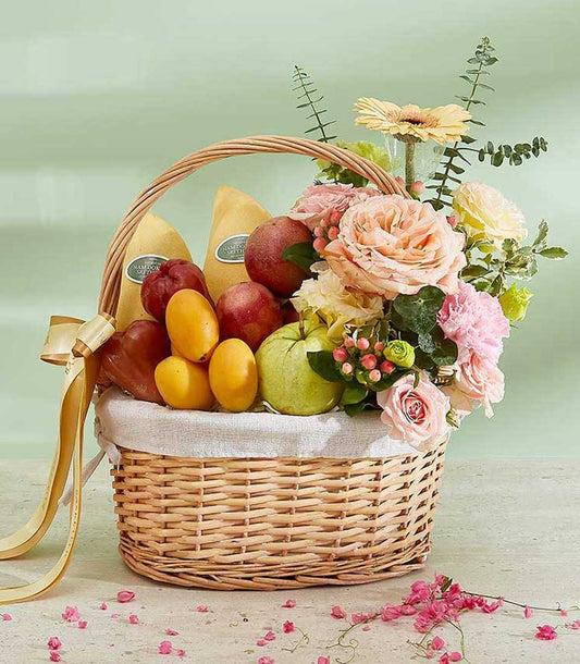 Wicker fruit basket with Thai mangoes, pomegranates, guava, peach roses, and pink carnations tied with gold ribbon