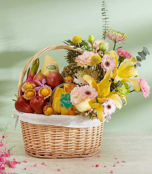 Woven wicker basket with fresh Thai tropical fruits, mango, dragon fruit, and flowers including yellow lilies and pink