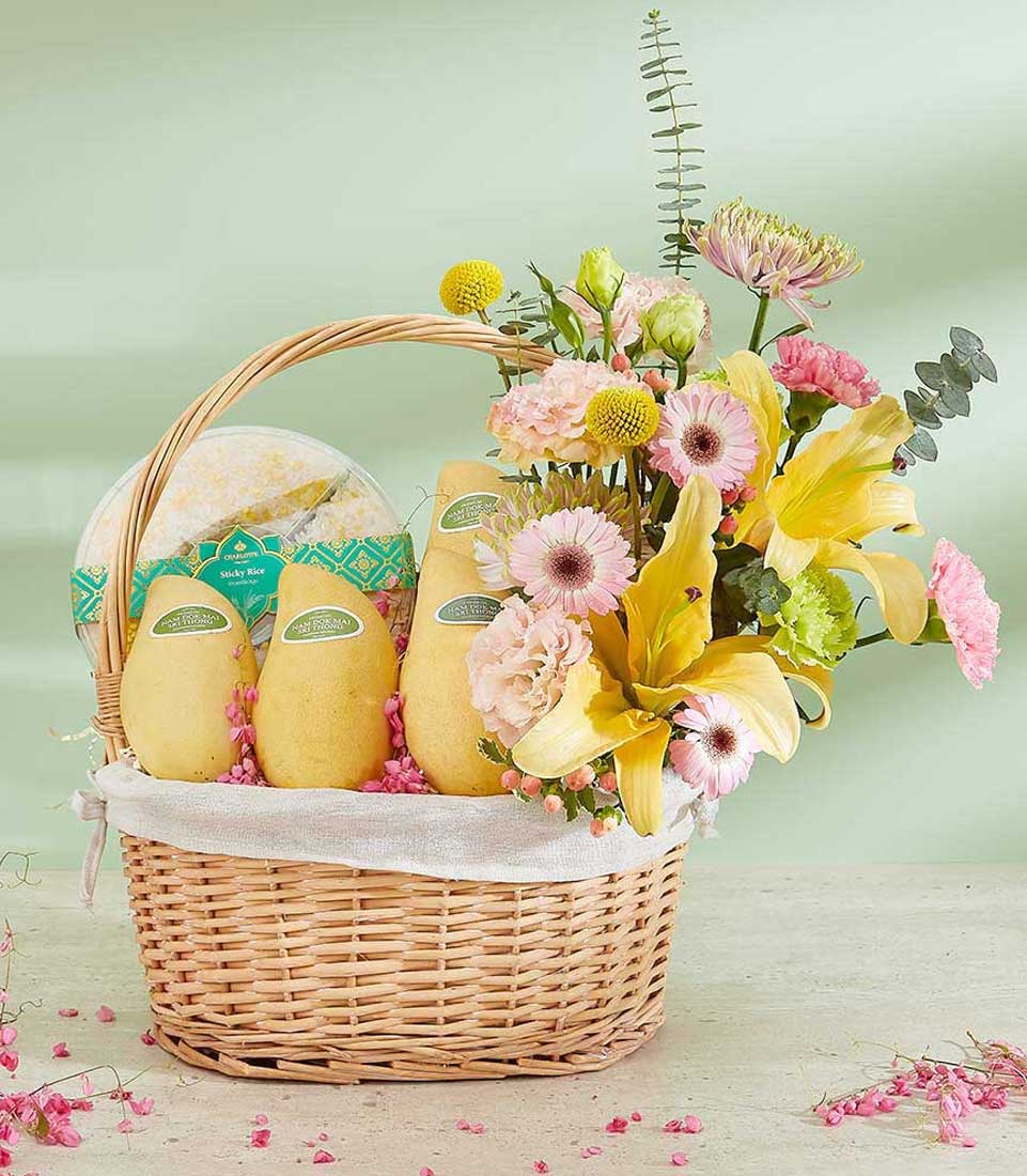 Wicker gift basket with fresh Thai mangoes, sticky rice, and vibrant yellow lily and pink gerbera bouquet