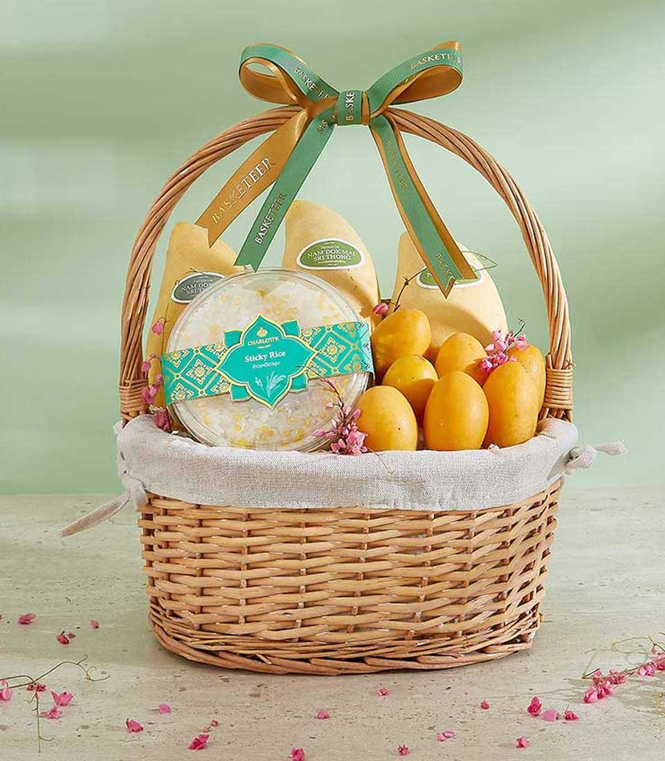 Woven wicker basket filled with golden mangoes, sticky rice, and fresh Thai tropical fruits with green and gold ribbon