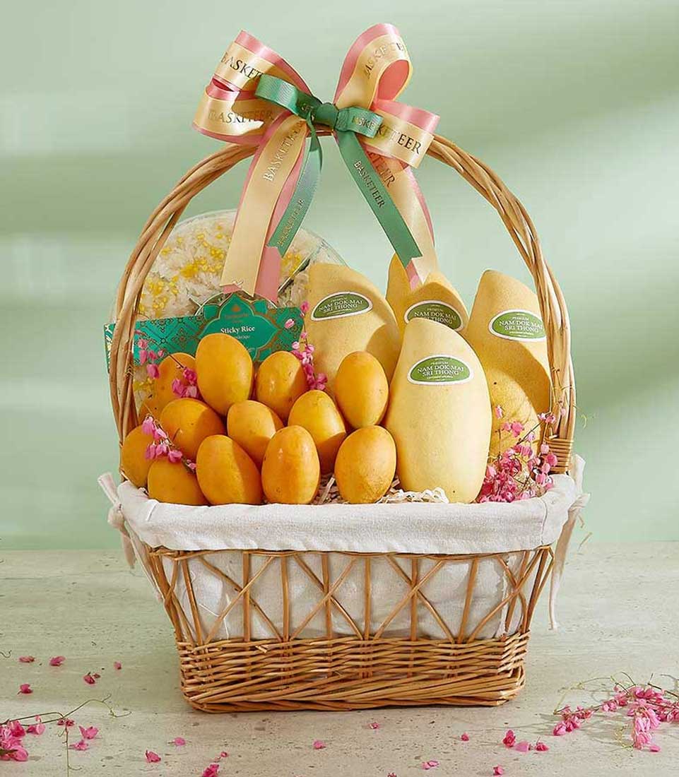 Tropical mango and sticky rice gift basket with woven wicker, pink flower petals, and Basketeer ribbon bow