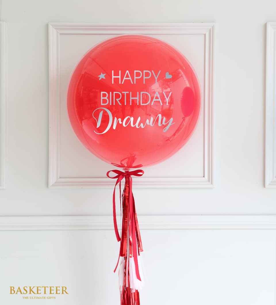 Red personalised balloon with silver "Happy Birthday" text, red and white tassel cluster, and satin bow