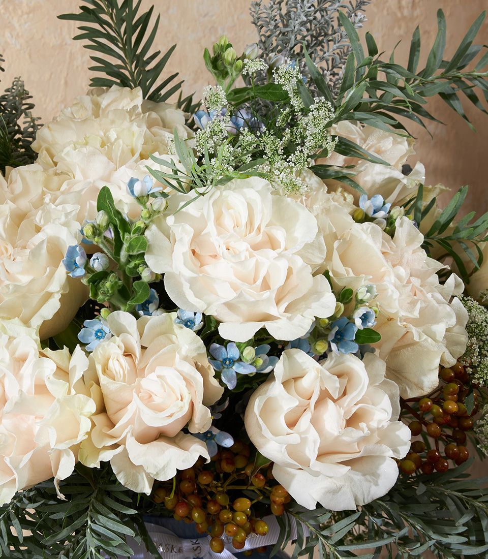 Cream and blush roses with light blue flowers in a soft blue vase arrangement