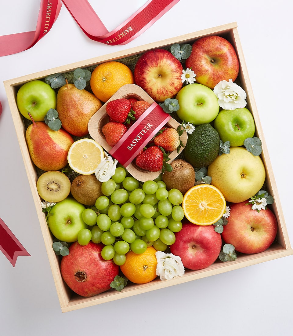Wooden luxury fruit gift box with fresh apples, pears, oranges, pomegranate, grapes, and strawberries with white flowers
