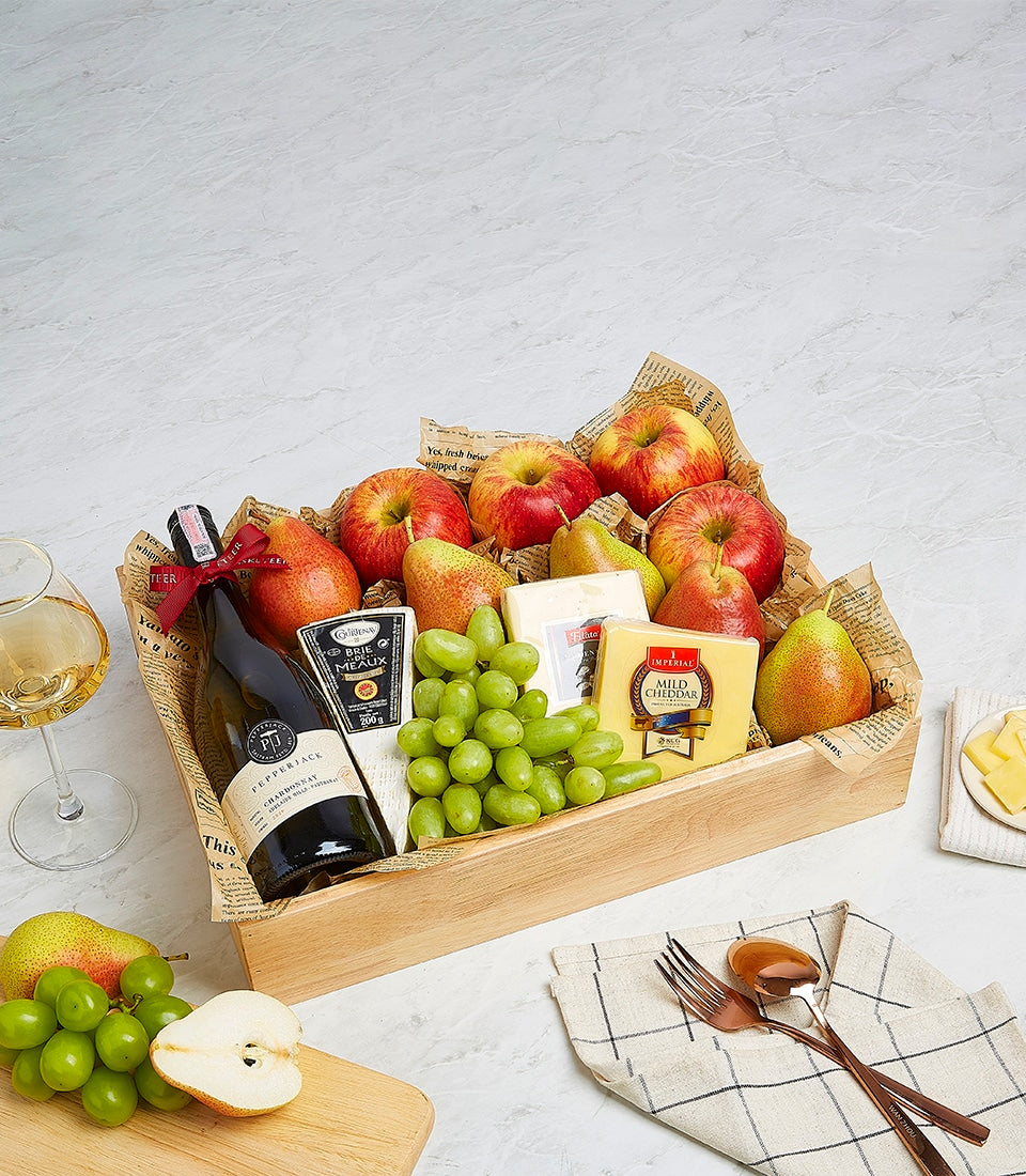 Wooden gift box with white wine, artisan cheeses, fresh apples, pears, and grapes on crumpled paper