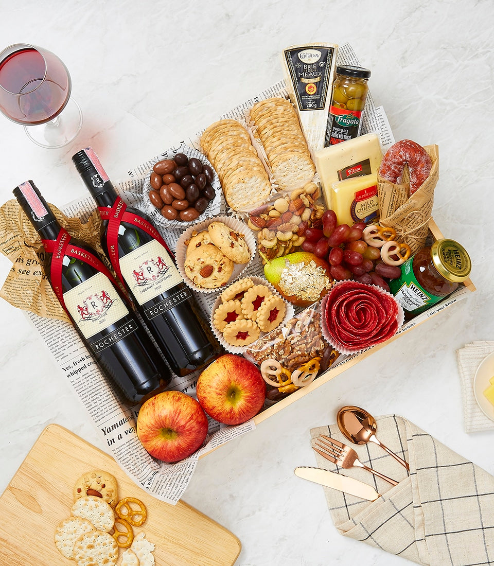 Gourmet wine gift hamper with two Rochester red wine bottles, aged cheeses, cured meats, crackers, nuts, and fresh fruit in