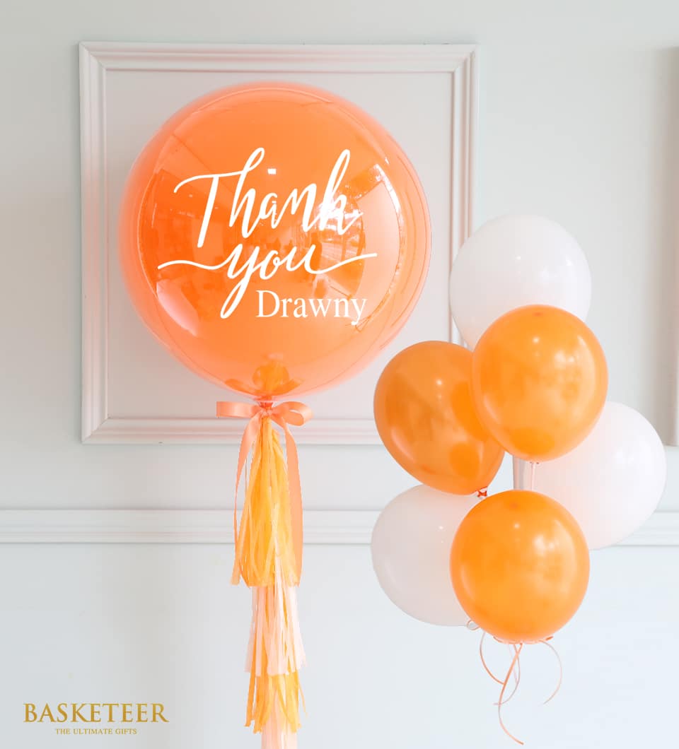 Orange and white balloon bouquet with personalized bubble balloon and tissue paper tassel for birthday celebrations