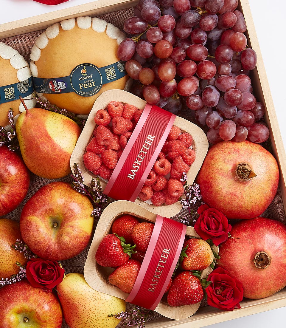 Wooden gift box filled with fresh pears, pomegranates, grapes, apples, raspberries, and strawberries with purple flowers and