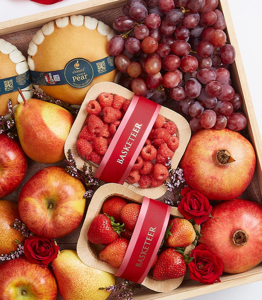 Wooden gift box filled with fresh pears, pomegranates, grapes, apples, raspberries, and strawberries with purple flowers and