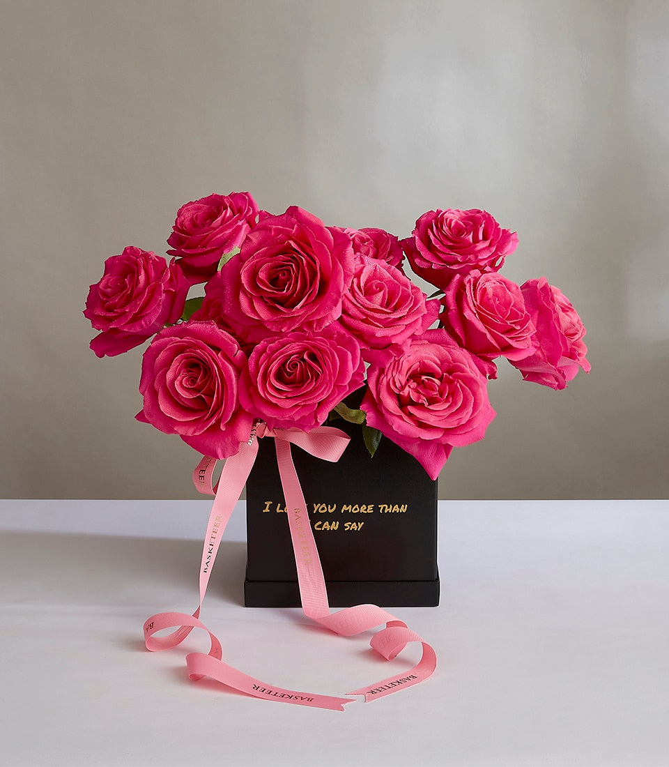 Vibrant fuchsia pink roses in sleek black luxury box with gold lettering, tied with pink ribbon
