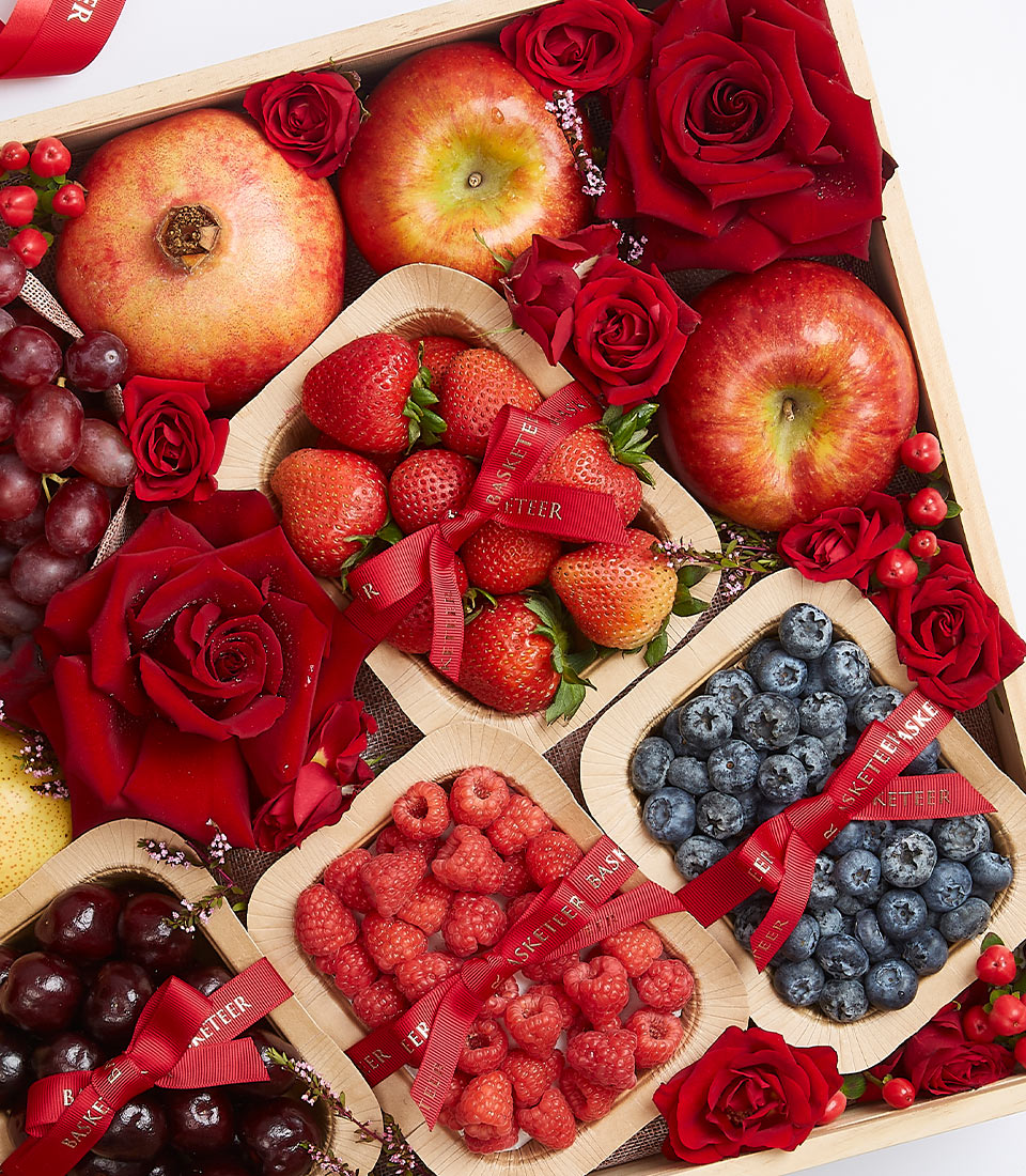 Wooden gift box with mixed berries, pomegranate, apples, fresh red roses, and artisan fruit containers with red ribbon