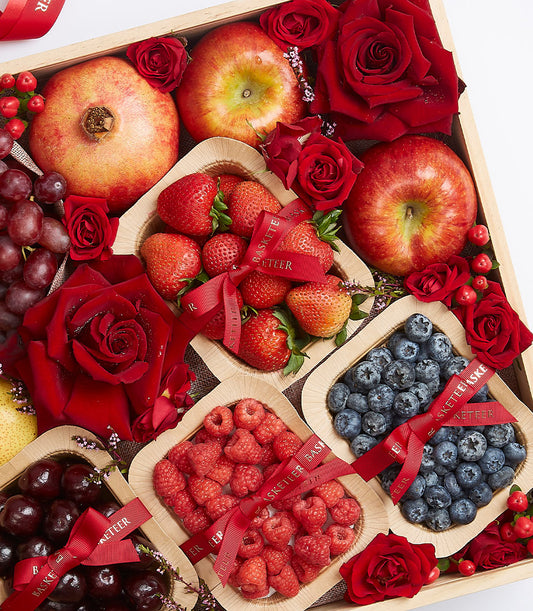 Wooden gift box with mixed berries, pomegranate, apples, fresh red roses, and artisan fruit containers with red ribbon