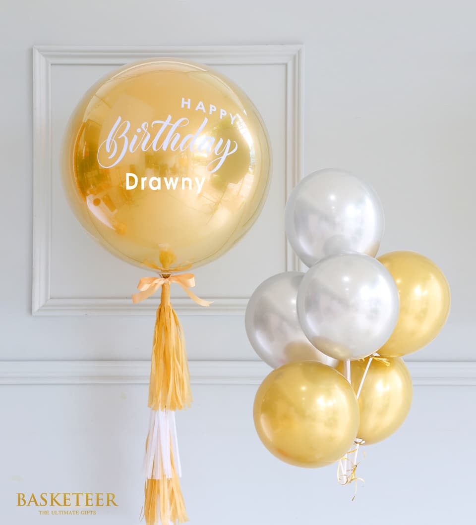 Gold bubble balloon with happy birthday message, gold and silver metallic balloon cluster, peach ribbon and tassel garland