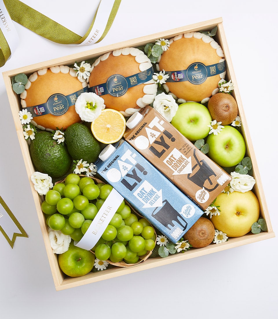 Wooden gift box with fresh pears, avocados, apples, kiwis, grapes, oat milk drinks, and white flowers