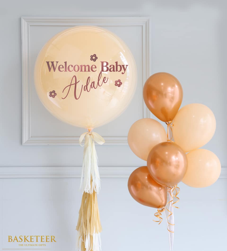 Peach bubble balloon personalized with baby name, tied with cream and gold ribbon, paired with matte peach and rose gold