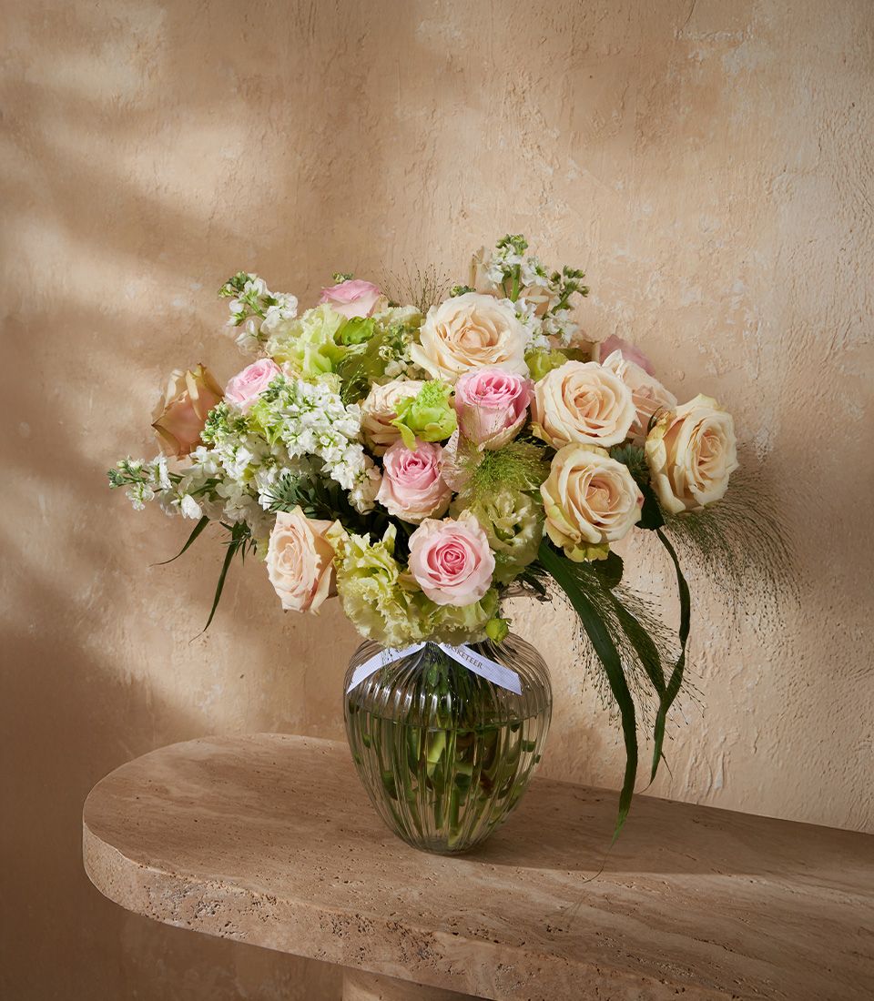 Blush pink and cream roses with white stock flowers in a clear ribbed glass vase