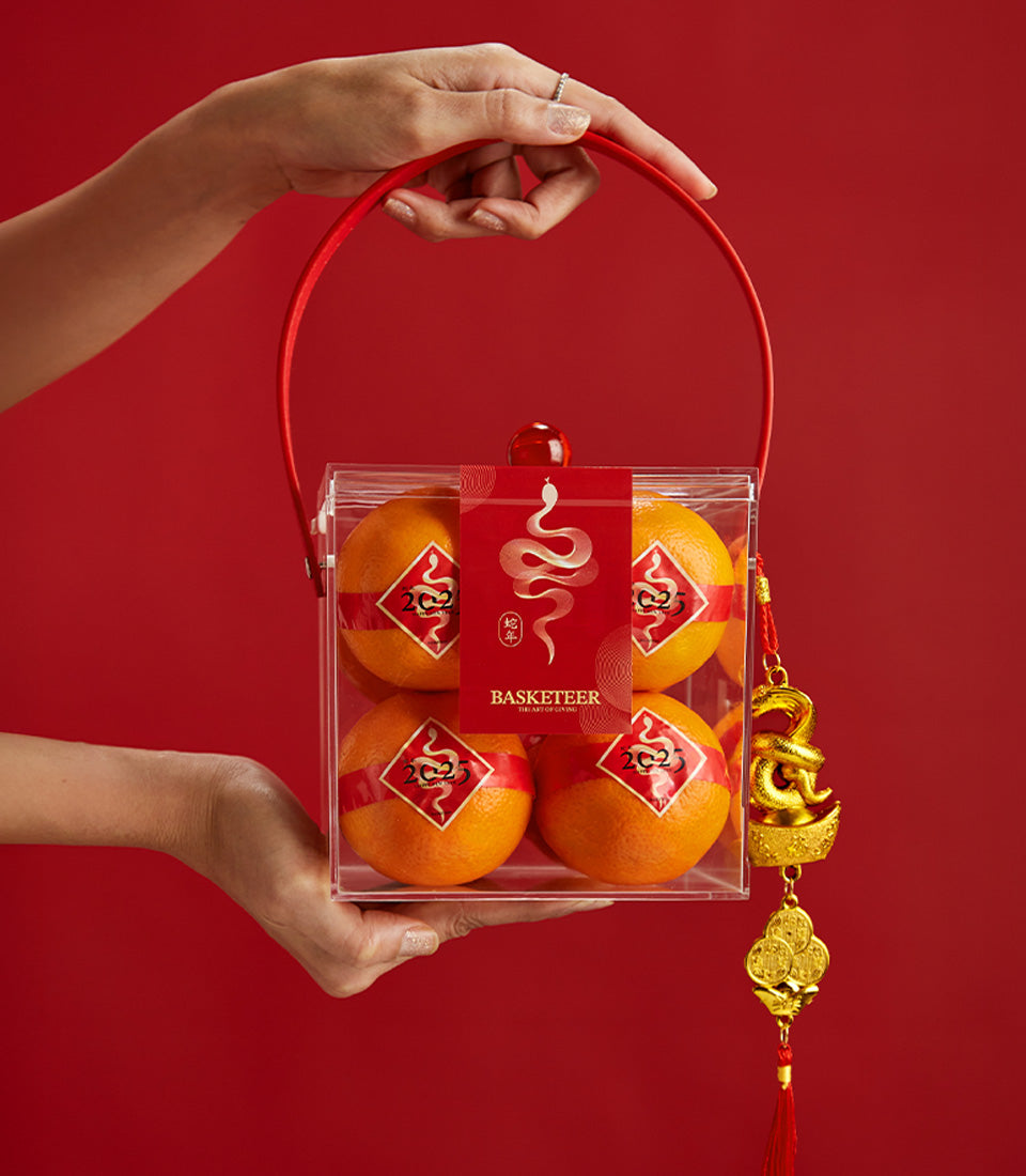 Premium mandarin oranges in acrylic gift box with red ribbon, gold snake charm, and Chinese New Year ornaments