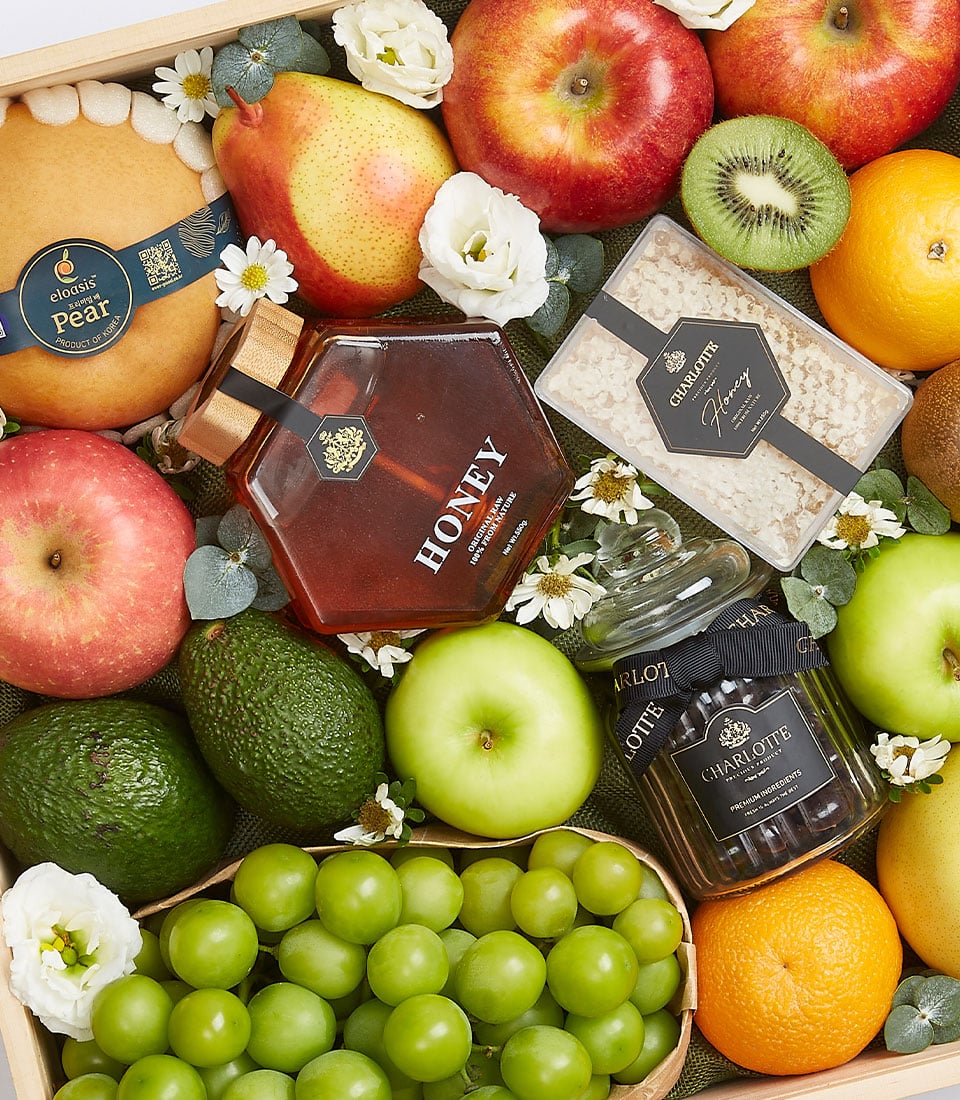 Premium fruit and honey gift box with apples, avocados, pear, grapes, and artisan honey on dark green fabric