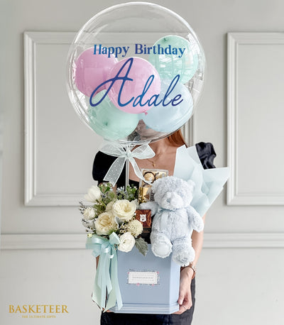 Pastel blue hexagonal gift box with white roses, teddy bear, chocolates, and birthday balloon bouquet