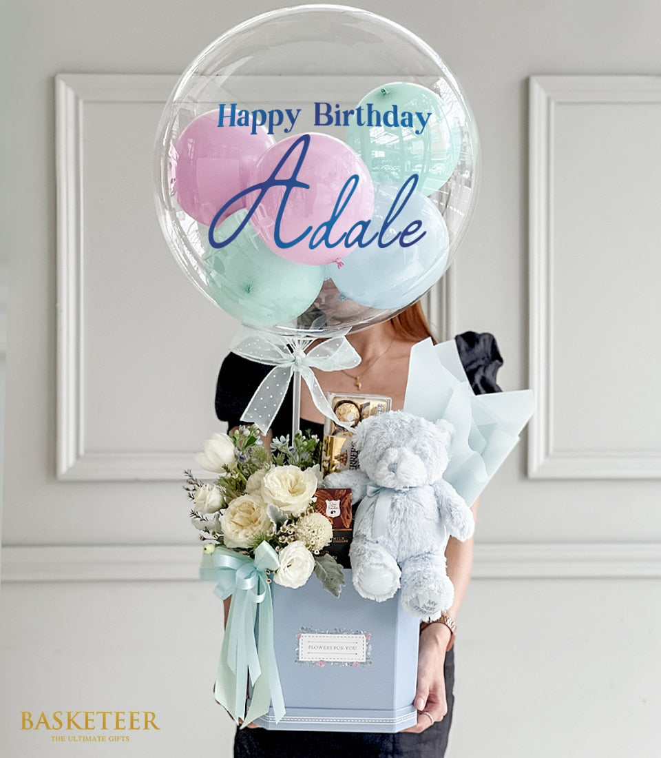 Pastel blue hexagonal gift box with white roses, teddy bear, chocolates, and birthday balloon bouquet