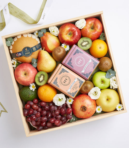 Wooden gift box with assorted fresh fruits, artisan tea tins, and decorative flowers on green fabric lining