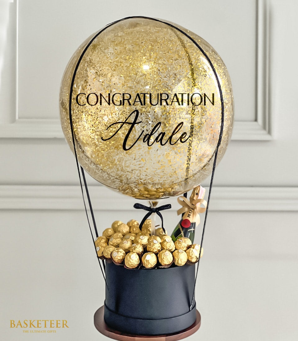 Luxury wine gift with gold balloon, champagne bottle, and gourmet chocolates in elegant black box