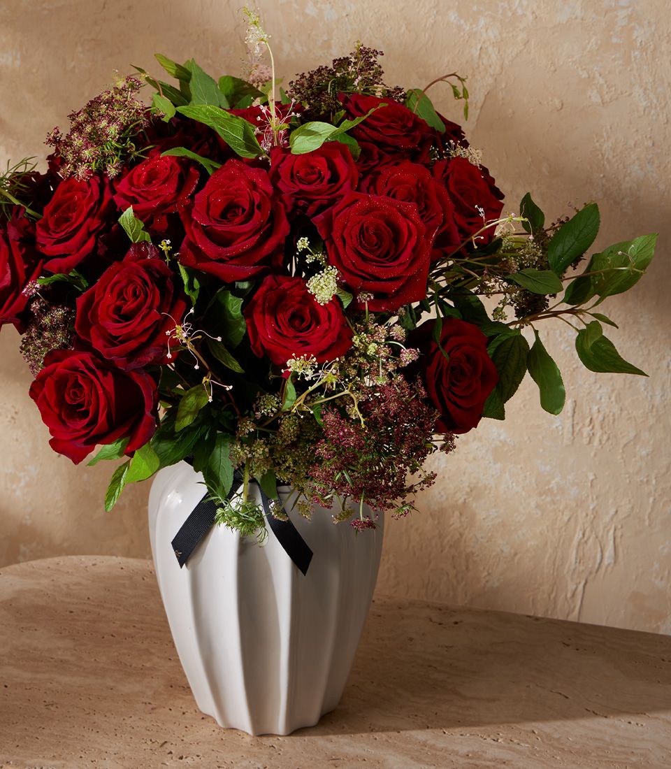 Deep red rose bouquet in white ceramic vase with black ribbon accent