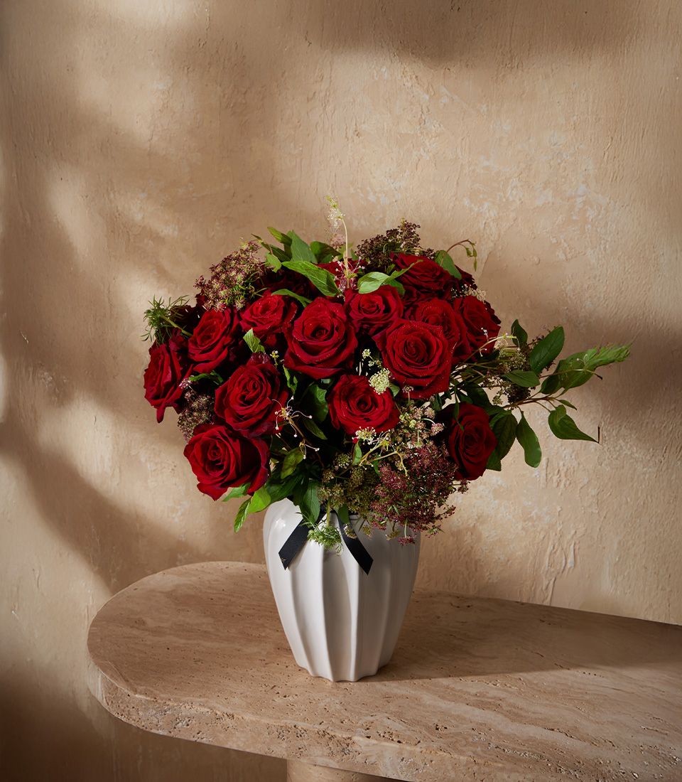 Deep red roses in white fluted vase with green foliage and black ribbon accent