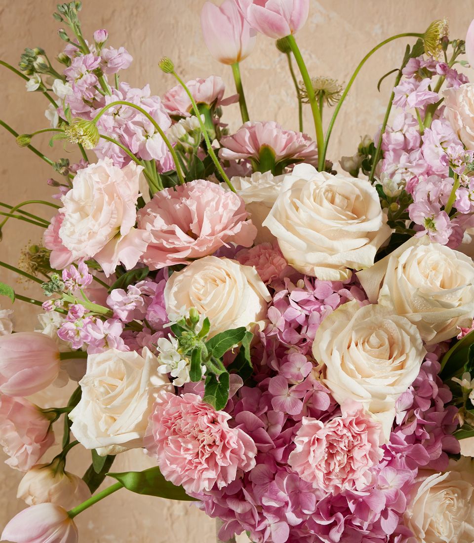 Pink and white rose vase arrangement with hydrangeas, carnations, and tulips in soft cream setting