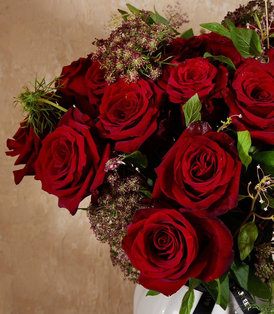 Deep red roses in white vase with delicate filler flowers and black ribbon