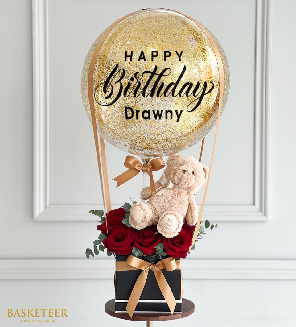 Gold glitter birthday balloon with red roses, teddy bear, and eucalyptus in luxury gift arrangement