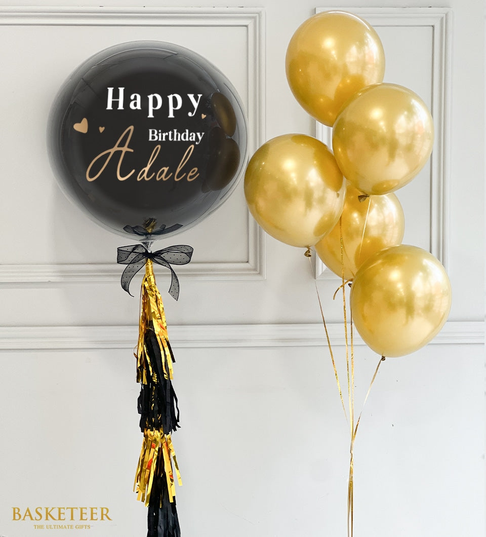 Black and gold Happy Birthday bubble balloon with personalized script, paired with gold metallic balloons and tassels