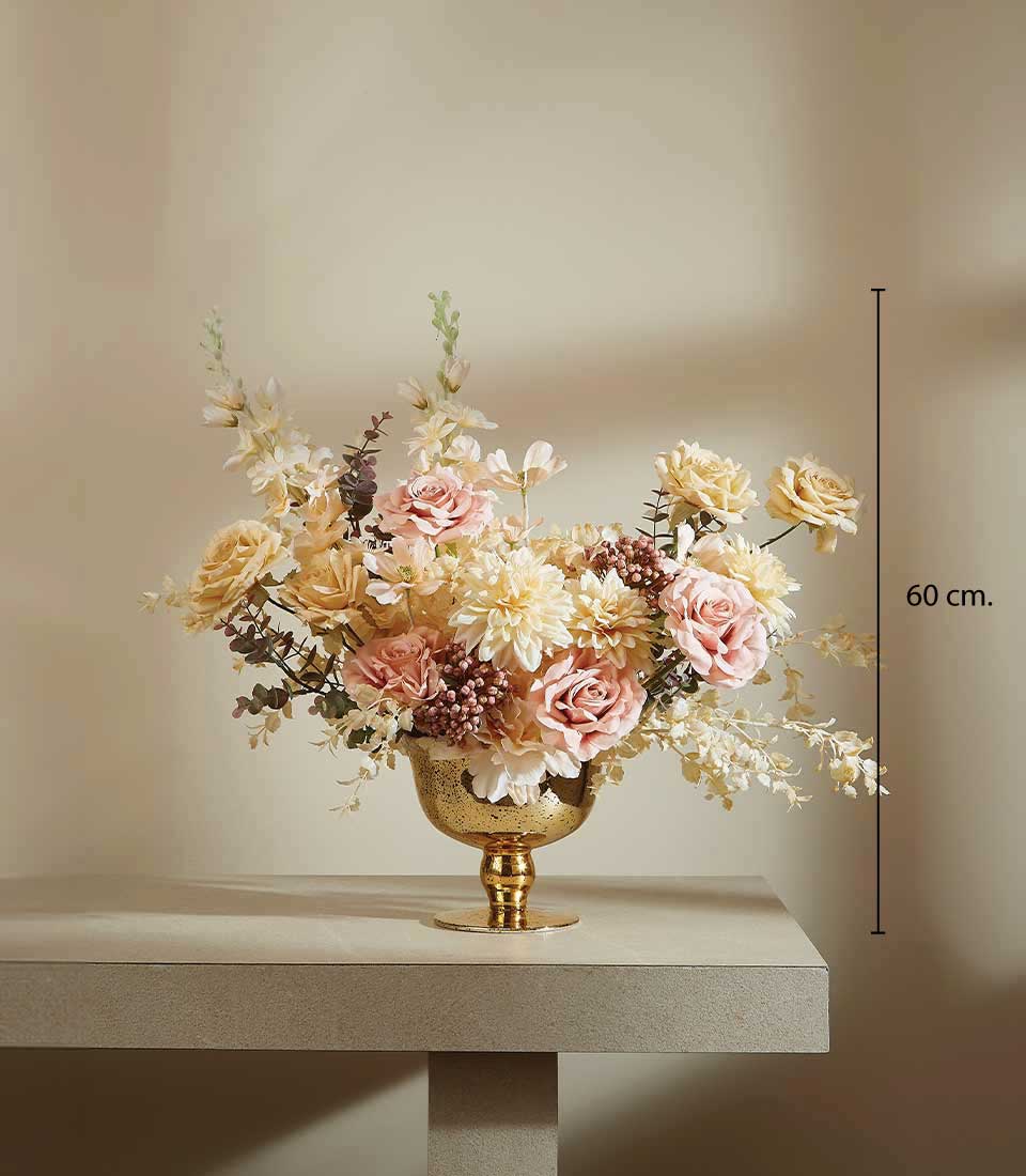 Tall artificial rose and dahlia arrangement in gold footed vase with peach, pink, and cream flowers