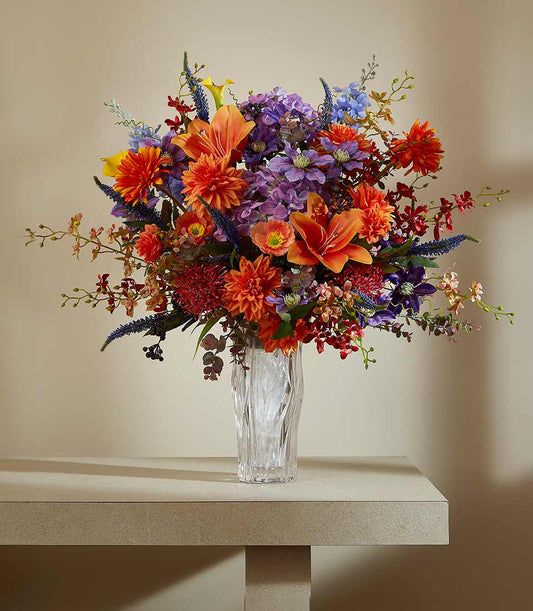 Vibrant artificial flower vase arrangement with orange lilies, purple hydrangeas, and red dahlias in textured glass