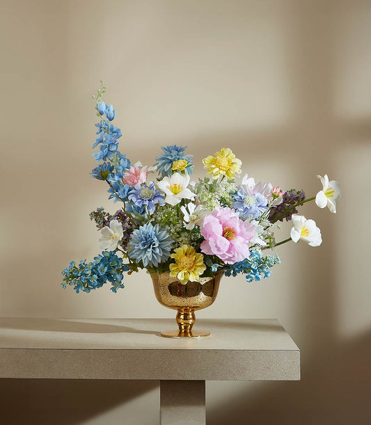 Vibrant springtime artificial flower arrangement with blue delphiniums, pink peonies, and yellow dahlias in gold textured