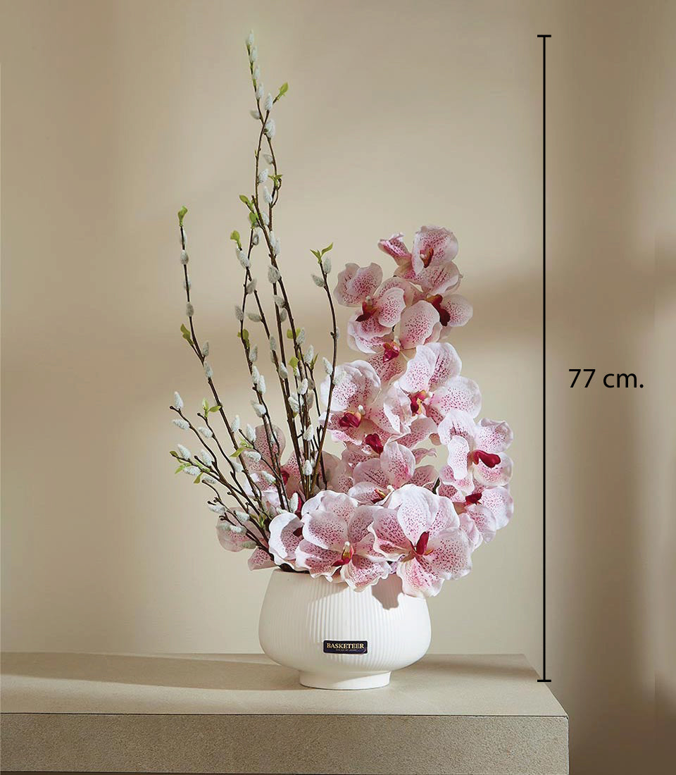 Light pink orchids with red centers and white catkin branches in white ceramic ridged vase, 77 cm tall