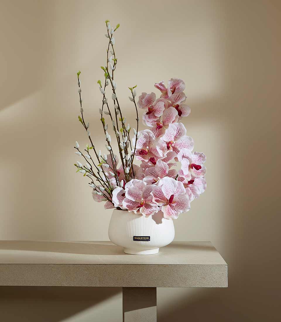 Light pink speckled orchids and pussy willow branches in white ceramic ridged vase
