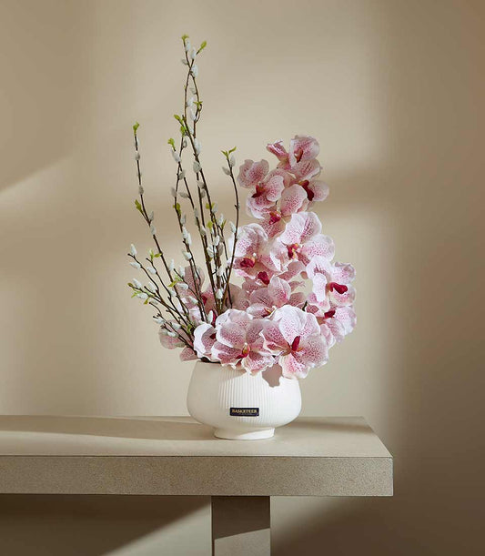 Light pink speckled orchids and pussy willow branches in white ceramic ridged vase