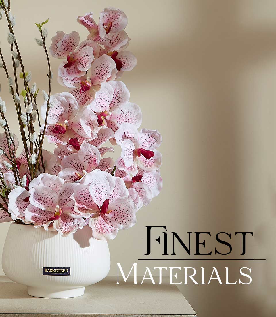 Light pink orchids with speckled centers and pussy willow branches in textured white ceramic vase