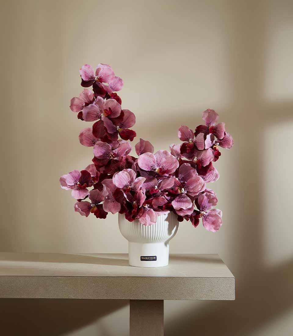 Elegant artificial orchid arrangement in white ribbed ceramic vase with magenta and pink blooms