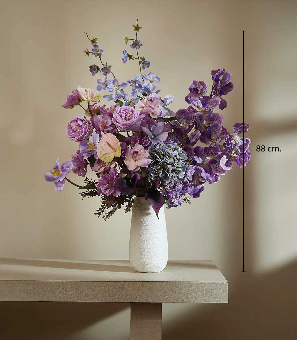 Tall purple and pink artificial flower arrangement with roses, orchids, and hydrangeas in textured white vase