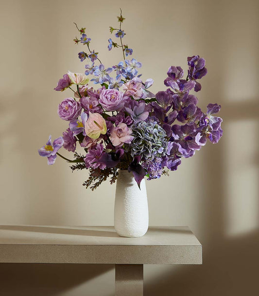 Lush purple and lavender artificial flower arrangement with orchids and roses in white textured vase