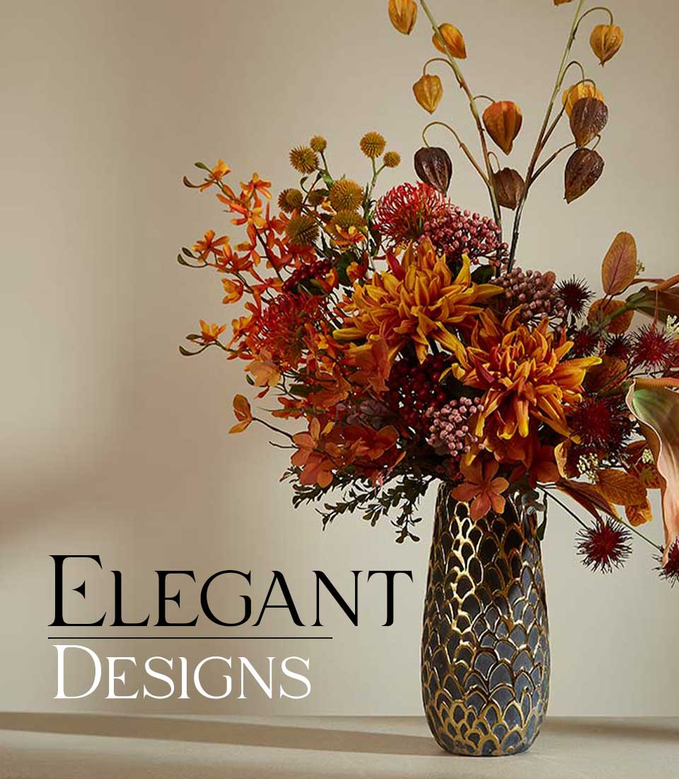 Autumnal artificial flower arrangement with orange dahlias, orchids, and dried seed pods in gold-patterned vase