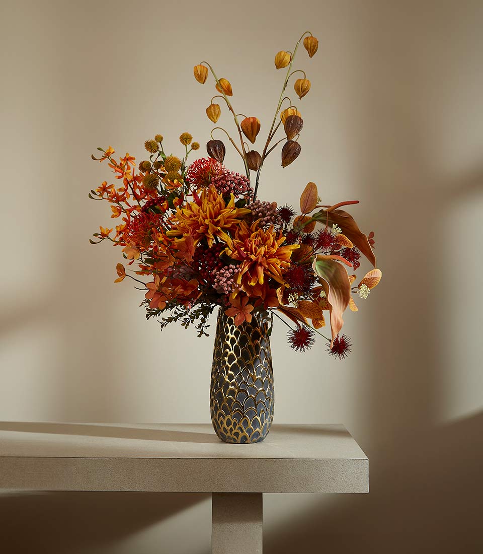 Autumnal floral arrangement with dahlias, protea, and Chinese lanterns in patterned grey vase