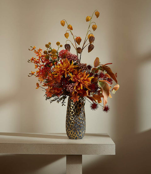 Autumnal floral arrangement with dahlias, protea, and Chinese lanterns in patterned grey vase