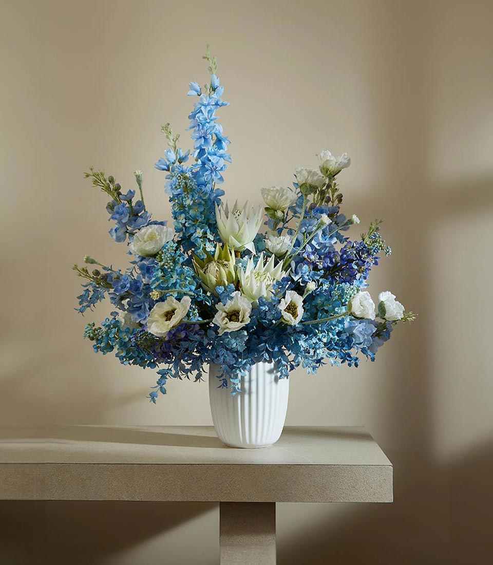 Serenity Blossom blue delphinium and white protea arrangement in fluted white vase