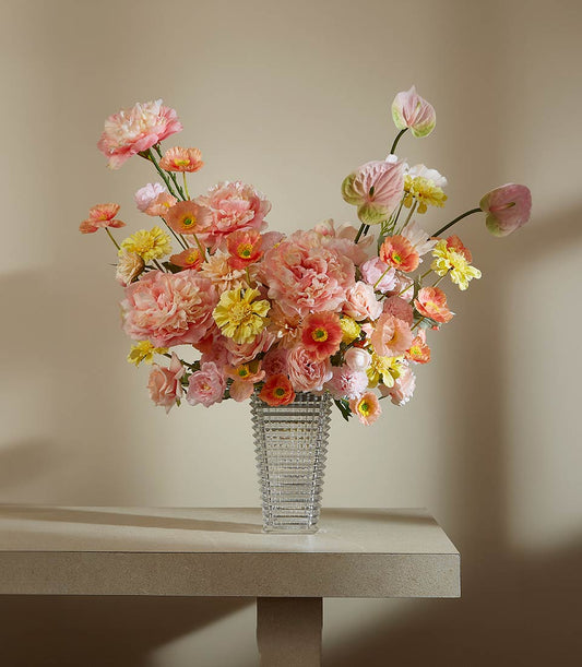 Vibrant peony and rose artificial flower arrangement in textured glass vase with pink, peach, and yellow blooms