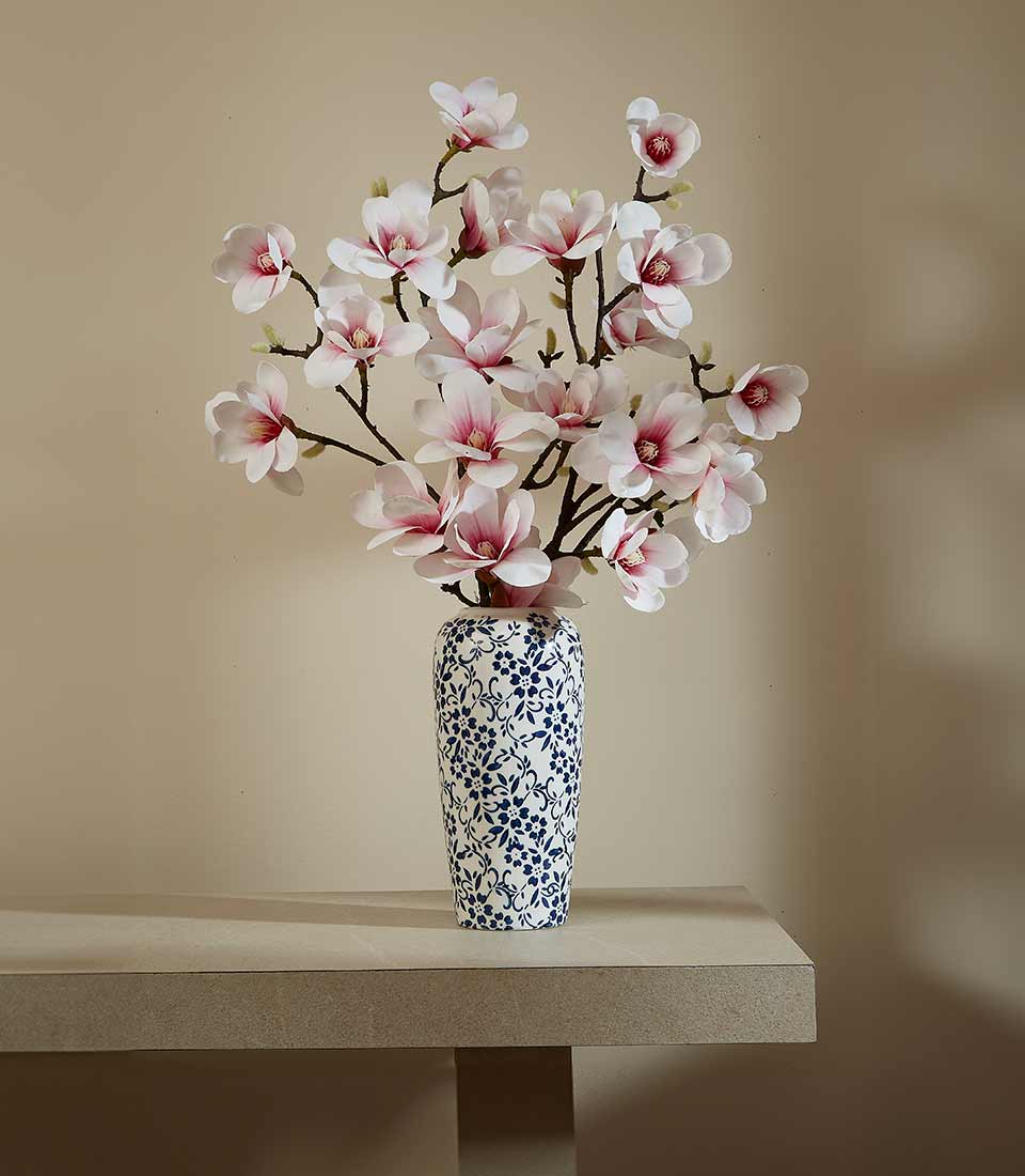 Tall blue and white ceramic vase with delicate pink magnolia artificial flowers and branch stems