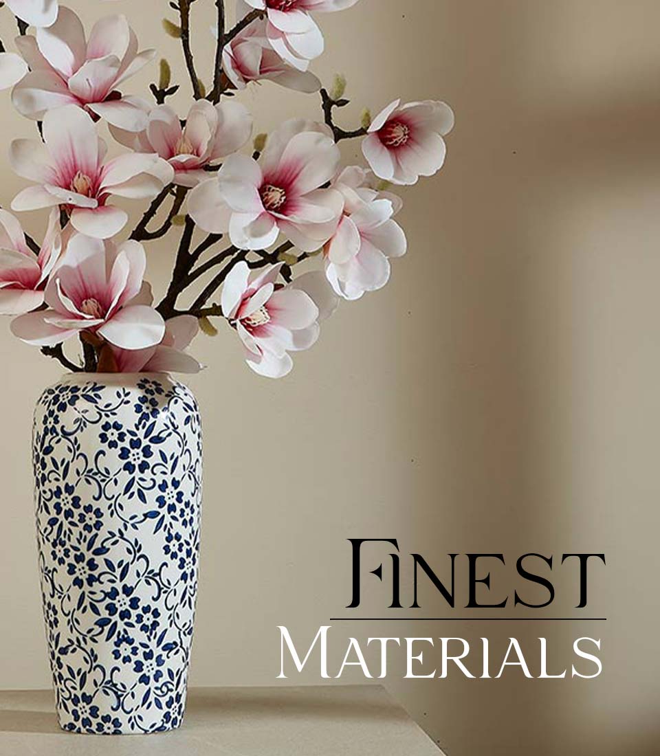 Tall white ceramic vase with blue floral pattern holding pink and white artificial magnolia flowers on brown stems